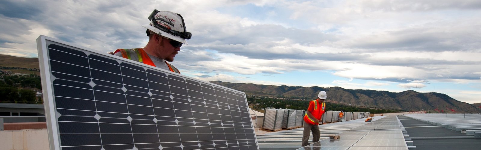 Instaladores de capacete e colete refletivo posicionando módulos fotovoltaicos em cobertura metálica